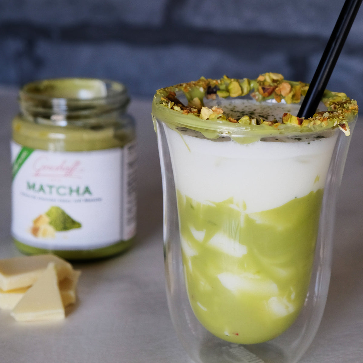 Matcha Eisschokolade im Glas. Im Hintergrund weiße Schokoladencreme mit Matcha von Grashoff.
