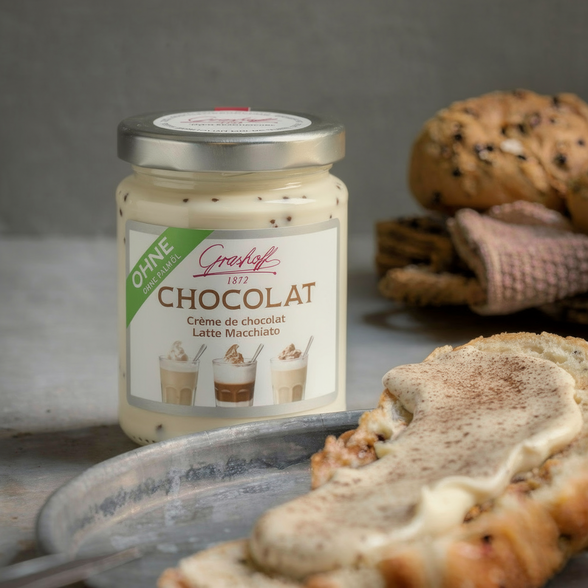 Ein Glas weiße Schokoladencreme mit Latte Macchiato Geschmack von Grashoff neben einem Brötchen.