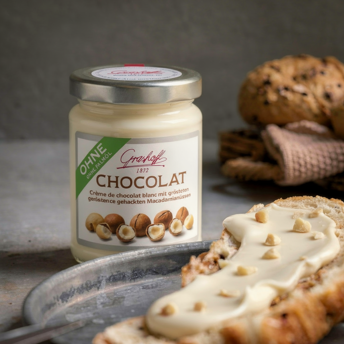 Ein Glas weiße Schokoladencreme mit Macadamia von Grashoff neben einem Brötchen.